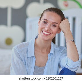 Young Woman Sitting On The Floor Near Children's Cot. Young Mom.