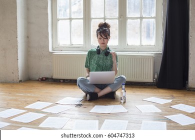 Young Woman Sitting On The Floor In A Rehearsal Studio, Using A Laptop Computer, Looking At Sheet Music