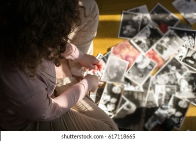 Young Woman Is Sitting On The Floor And Looking At Old Photographs