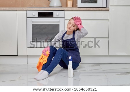 Young woman sitting on the floor tired after cleaning. Large modern kitchen. Routine chores.