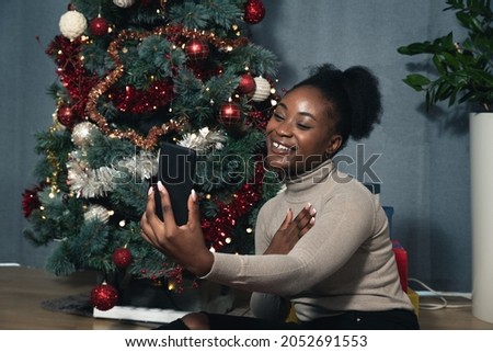 Young woman sitting on the floor at home in front of a Christmas tree talks online on video call with boyfriend a soldier in the army who will not be able to be at home during the New Year holidays 