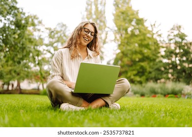 Young Woman sitting on green grass ground, working on laptop in city park.  Mobile Office. Concept for education, business, blog or freelance. - Powered by Shutterstock