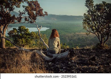 A young woman is sitting on a hill damaged by wild fires at sunrise
