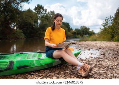 A young woman is sitting on a kayak, holding a paper map and check the route. Copy space. The concept of the World Tourism Day.