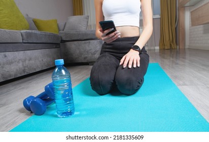 Young Woman Sitting On Mat Holding Smartphone. Watching Online Workout