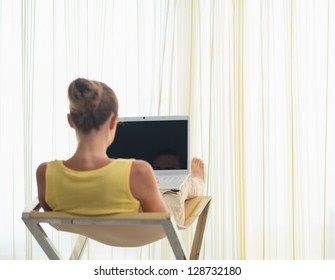 Young Woman Sitting On Modern Chair With Laptop. Rear View