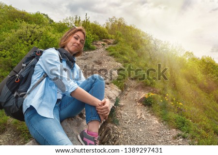 A young Woman sitting on a mountain stone path and posing for the camera. Sun light. Bottom view.