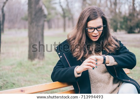 Young woman sitting on a park bench and checks the time on a wristwatch