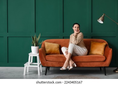 Young woman sitting on red sofa near green wall - Shutterstock ID 2243405167