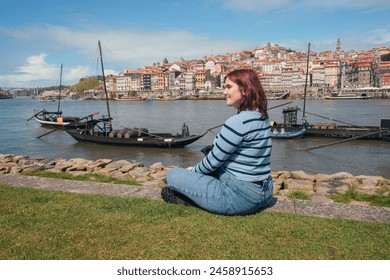 Young woman sitting on riverside in Porto, Portugal overlooking traditional boats and cityscape - Powered by Shutterstock