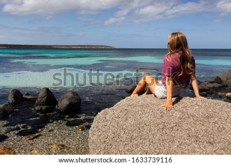 Young woman sitting on a rock by the sea with view of beautiful coastline on sunny day on the Eyre Peninsula, South Australia