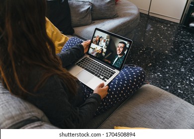 Young Woman Sitting On The Sofa With Her Legs Crossed Makes A Group Video Call With The Laptop With Her Millennial Friends, A Man On The Piano, A Mom With A Baby Girl At Park And Three Muslim Friends