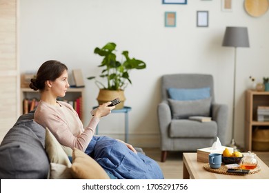 Young woman sitting on sofa with control remote and watching TV she has a cold and stay at home - Shutterstock ID 1705291756