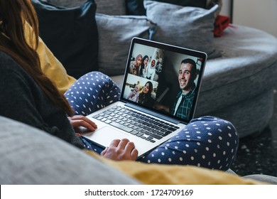 Young Woman Sitting On The Sofa With Her Legs Crossed Makes A Group Video Call With The Laptop With Her Millennial Friends, A Man On The Piano, A Mom With A Baby Girl At Park And Three Muslim Friends