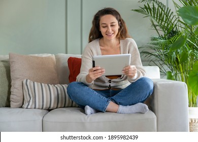 Young woman sitting on sofa and using tablet pc. Watching movies on the internet.