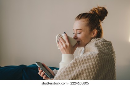 Young woman sitting on the sofa with plaid, drinking coffee, relaxing in her living room. Happy lifestyle. Beauty portrait. - Powered by Shutterstock