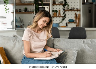 Young woman sitting on the sofa writing down the guest list of her friends whom she will invite to her bachelorette party for her wedding. Creative girl writes down ideas make a list of things to do - Powered by Shutterstock