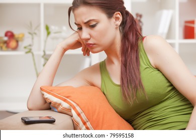young woman sitting on sofa and looking at phone, waiting for the call