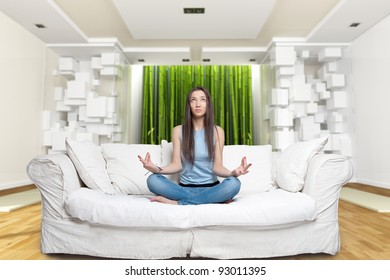 Young woman sitting on a sofa in the lotus position meditating in a zen environment
