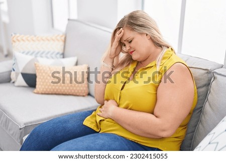 Young woman sitting on sofa suffering for head and stomach ache at home