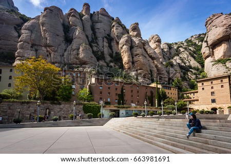 Young woman is sitting on steps among buildings of Montserrat monastery located between huge rocks in Catalonia, Spain