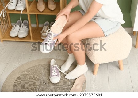 Young woman sitting on stool and putting orthopedic insoles into gumshoes