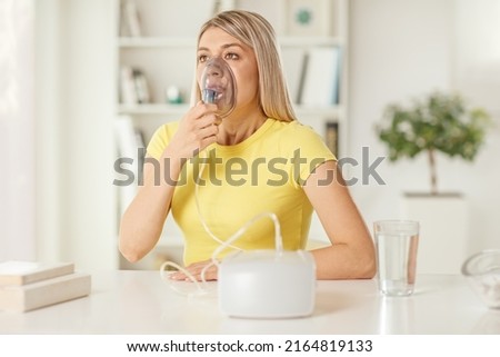 Young woman sitting on a table and using an inhaler at home