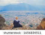 Young woman sitting on top of cliff in summer mountains at sunset and enjoying beautiful view of nature landscape cityscape. Monastery Meteora Kalambaka town in Greece Europe. Wanderlust adventure