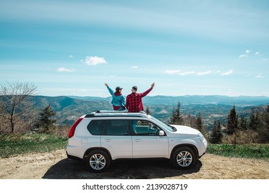 young woman sitting on the top of the suv car at mountain peak enjoying the landscape view at summer sunny day