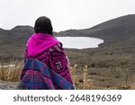 A Young woman sitting on a viewpoint into colombian sumapaz paramo with clkoudy sky at background