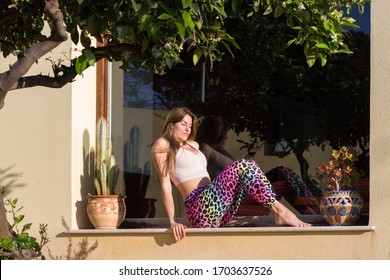 Young woman sitting on windowsill sunbathing on summer day