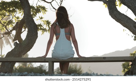 Young woman sitting on a wooden fence, enjoying the ocean view and nature, feeling peaceful and calm in a tropical paradise - Powered by Shutterstock