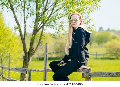 Young Woman Sitting On The Wooden Fence In The Country Side 