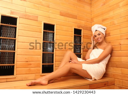 Young woman sitting on wooden bench in infrared sauna, space for text. Spa treatment