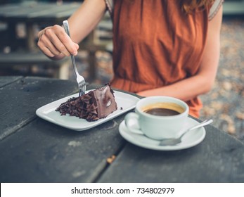 A Young Woman Is Sitting Outside Drinking Coffee And Eating Cake