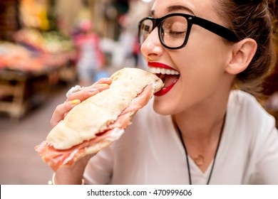 Young woman sitting with panini sandwich with prosciutto at the cafe outdoor on the street in Bologna city