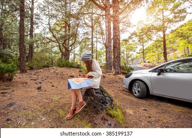 Young Woman Sitting With Paper Map Near The Car In The Forest