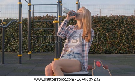 A young Woman is sitting in a Park and drinking water from a bottle.