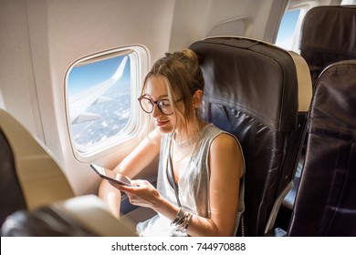 Young Woman Sitting With Phone On The Aircraft Seat Near The Window During The Flight In The Airplane