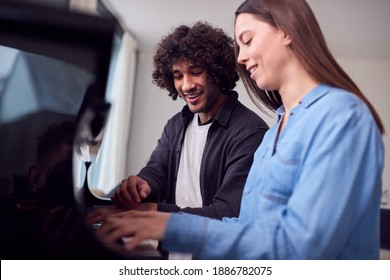 Young Woman Sitting At Piano Having Lesson From Male Teacher