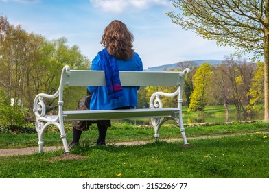 Young woman sitting and relaxing on the white bench in a castle park by the river on a sunny spring day