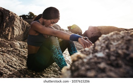 Young woman sitting rocks outdoors after her workout and looking down. Female athlete taking rest after fitness training. - Powered by Shutterstock