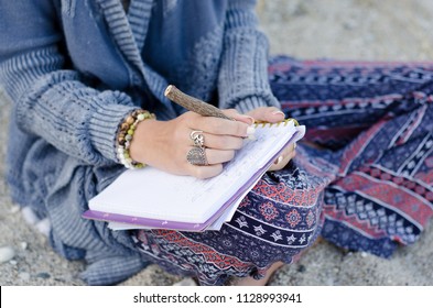 Young Woman Sitting In Sand On Beach Writing In Journal