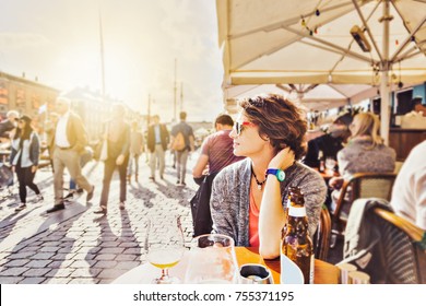Young woman sitting in a street cafe drinking beer and watching the city life, Europe lifestyle. Denmark, Copenhagen, Nyhavn
