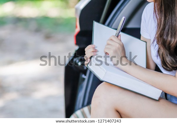 The young woman is sitting studying the Bible on\
the back of her car in the park alone because he wants to learn the\
Bible to understand and take notes to come back to understand the\
Bible again.