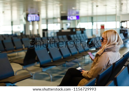 Young woman sitting in the terminal waiting room and waiting for departure, she is texting and connecting with her smartphone