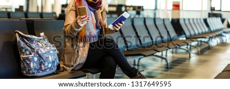 Young woman sitting in the terminal waiting room and waiting for departure, she is texting and connecting with her smartphone