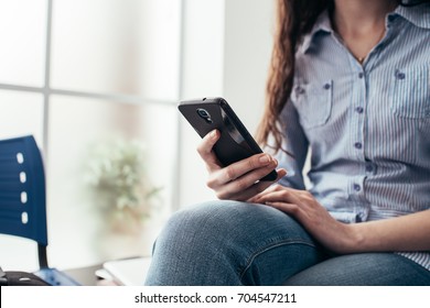 Junge Frau im Wartezimmer und SMS mit ihrem Smartphone