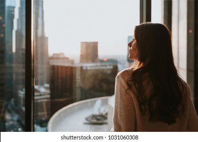  Young woman sitting at window  enjoying the city skyline from the 35 floor at sunset with stunning panoramic view of Los Angeles.