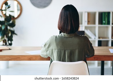 Young Woman Sitting At Wooden Desk And Working In Modern Minimalist Office. Back View